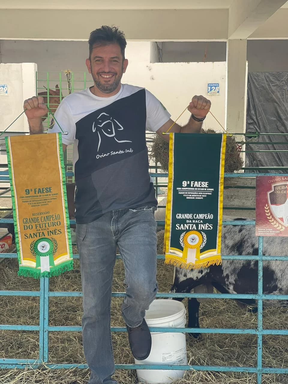 Augusto Cesinha na baia, segurando duas faixas de premiação da raça Santa Inês